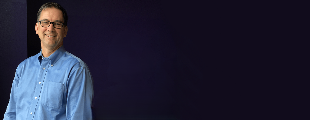 UW Internal Audit Executive Director Richard Cordova standing in front of a dark purple wall.