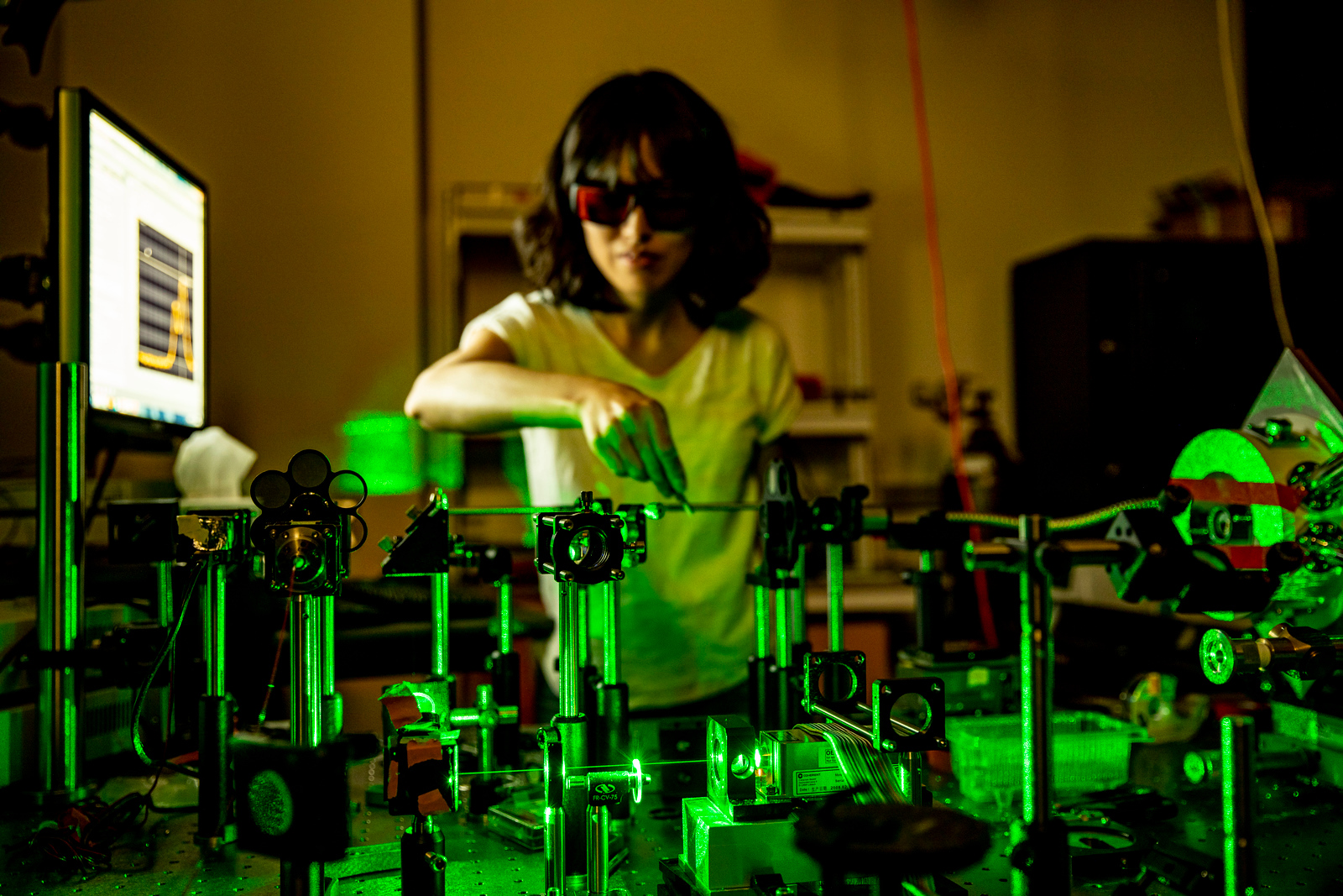 A woman in dark glasses works with an array of lab equipment lit in bright green