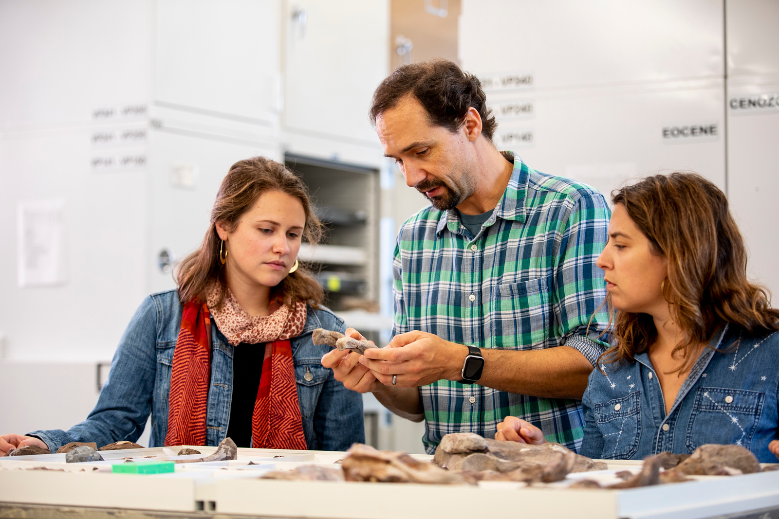 A man and two women examine fossils in a brightly lit lab