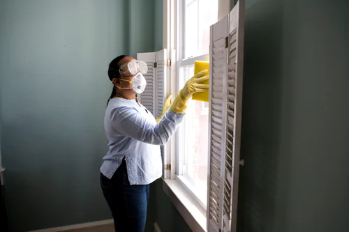 woman in protective gear cleaning a window with a sponge
