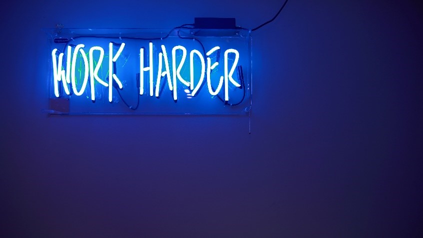 neon sign reading WORK HARDER 