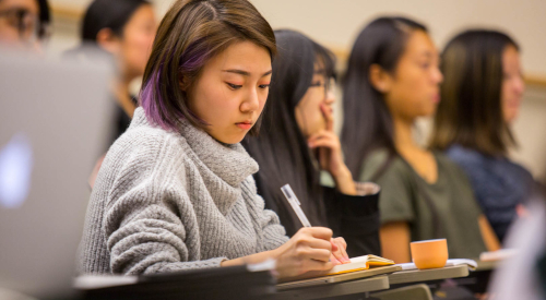 student with streak of purple hair taking notes during class